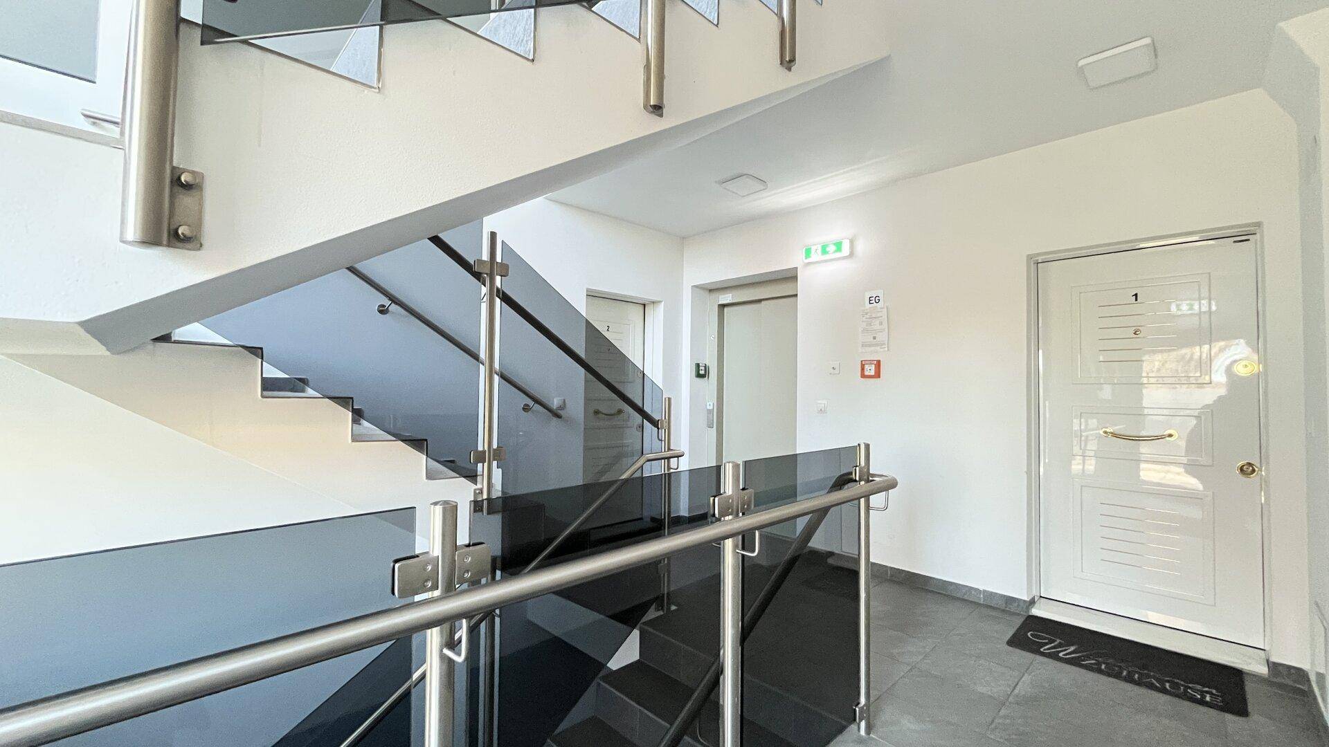 Modernes Treppenhaus mit Glasgeländer und Aufzug für barrierefreien Zugang.