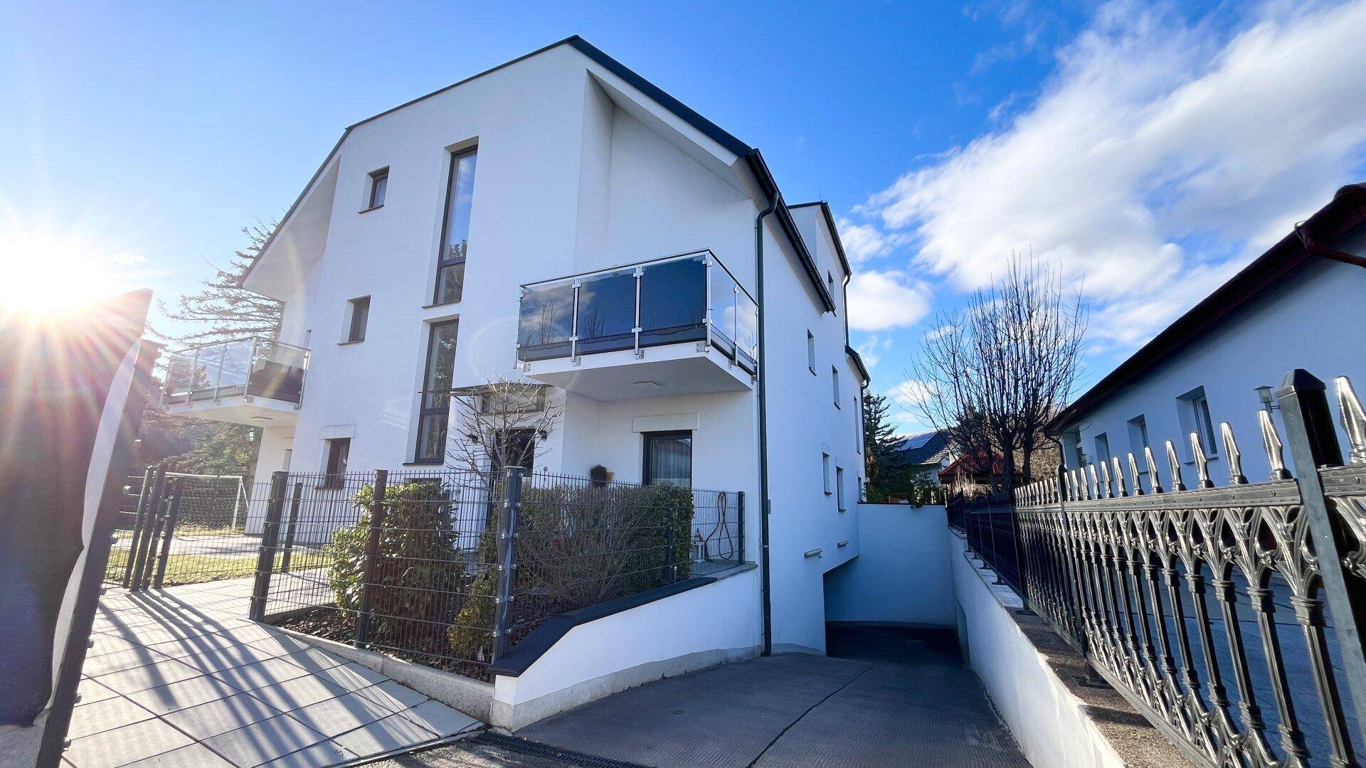 Moderne Wohnanlage mit weißer Fassade, Balkonen und Zufahrt.