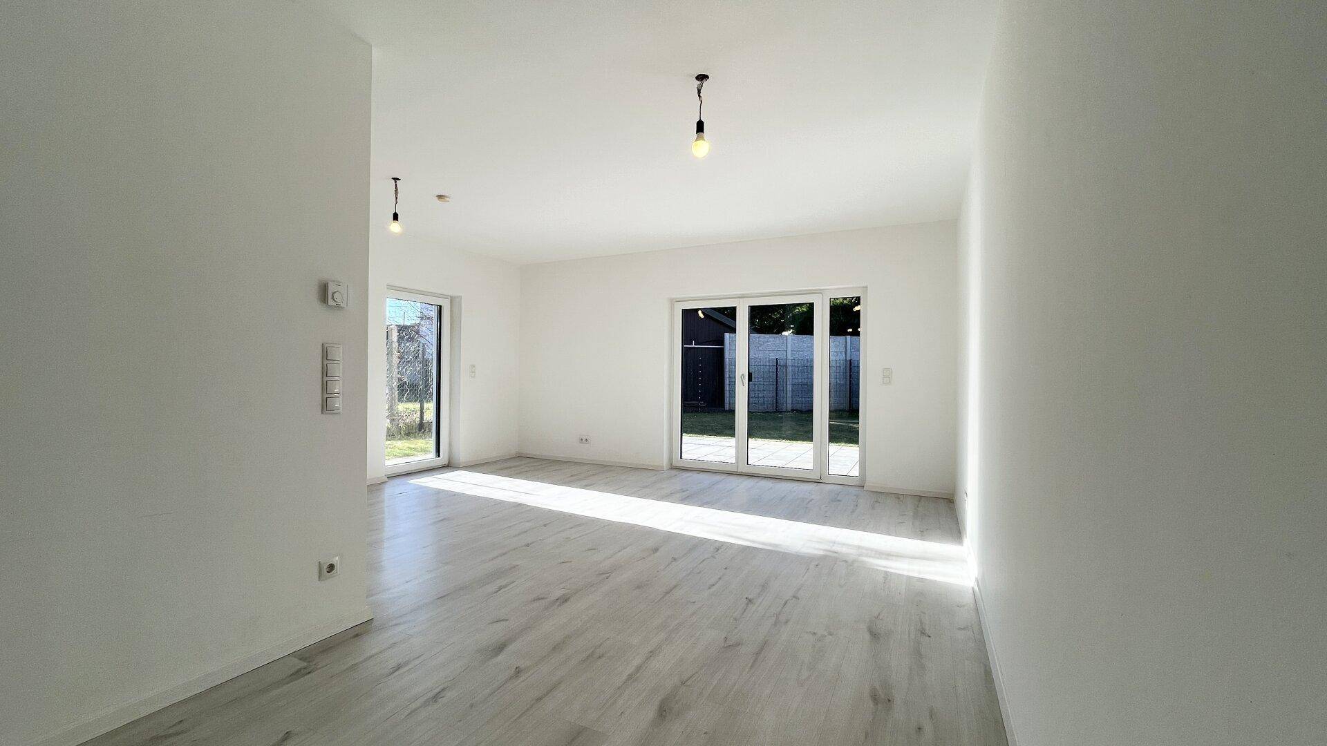 Geräumiges, helles Wohnzimmer mit Laminatboden und Schiebetüren zum Außenbereich.