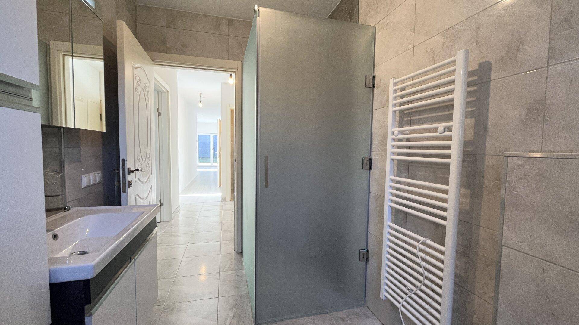 Modernes Badezimmer mit Fliesenboden, Waschtisch und Duschkabine aus Glas.