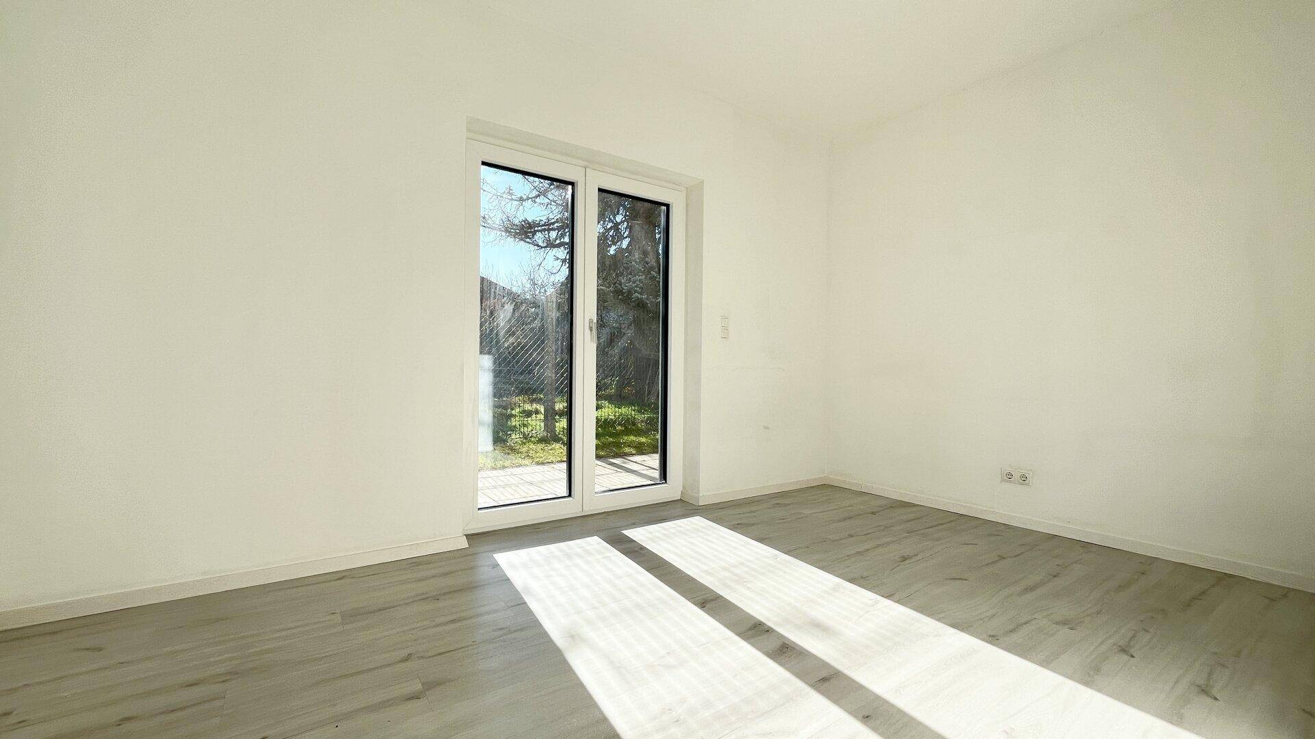 Helles Schlafzimmer mit Laminatboden und großen Schiebetüren zum Garten.
