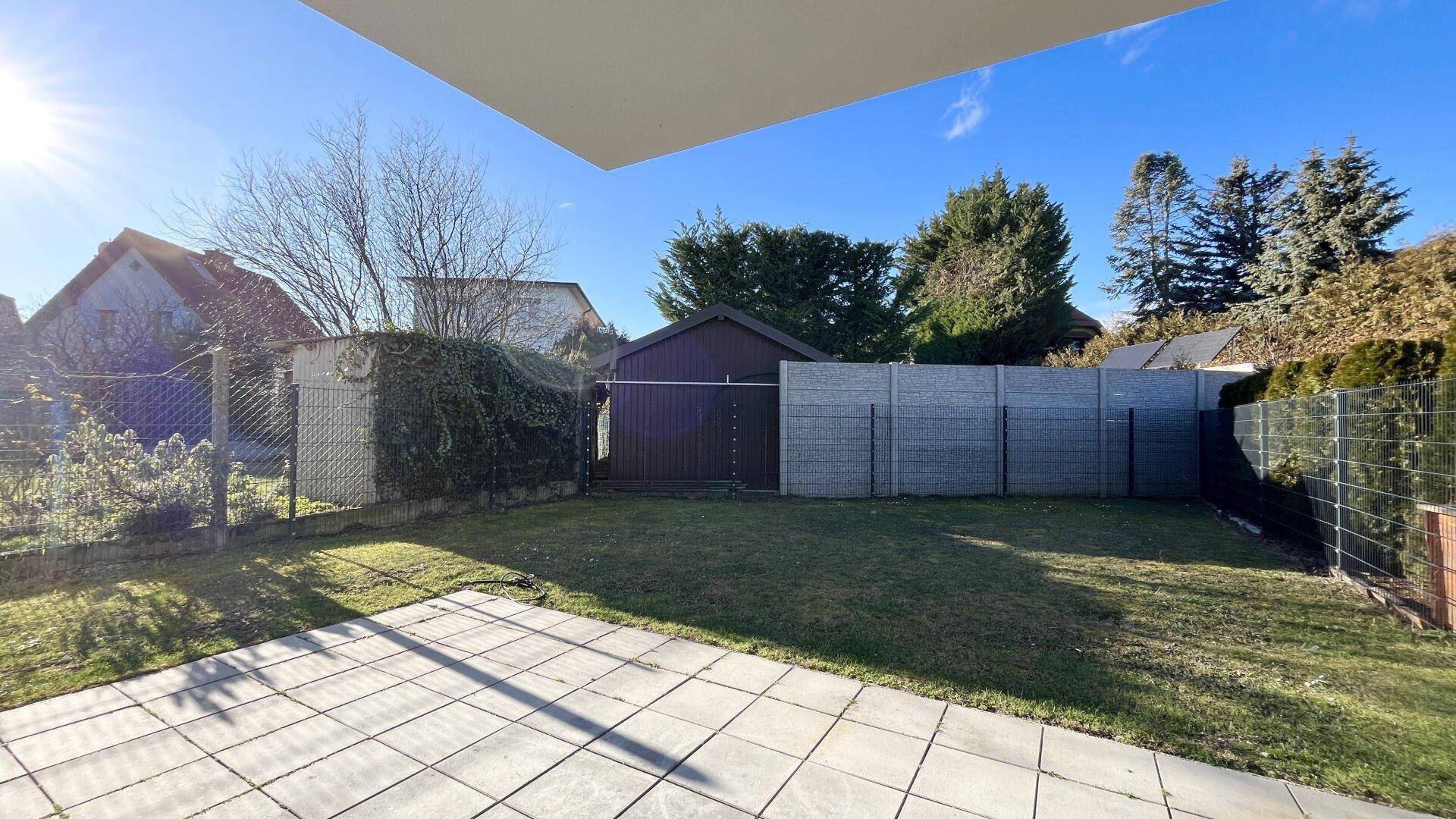 Sonniger Gartenbereich mit Rasenfläche, Gartenhaus und umlaufendem Zaun.