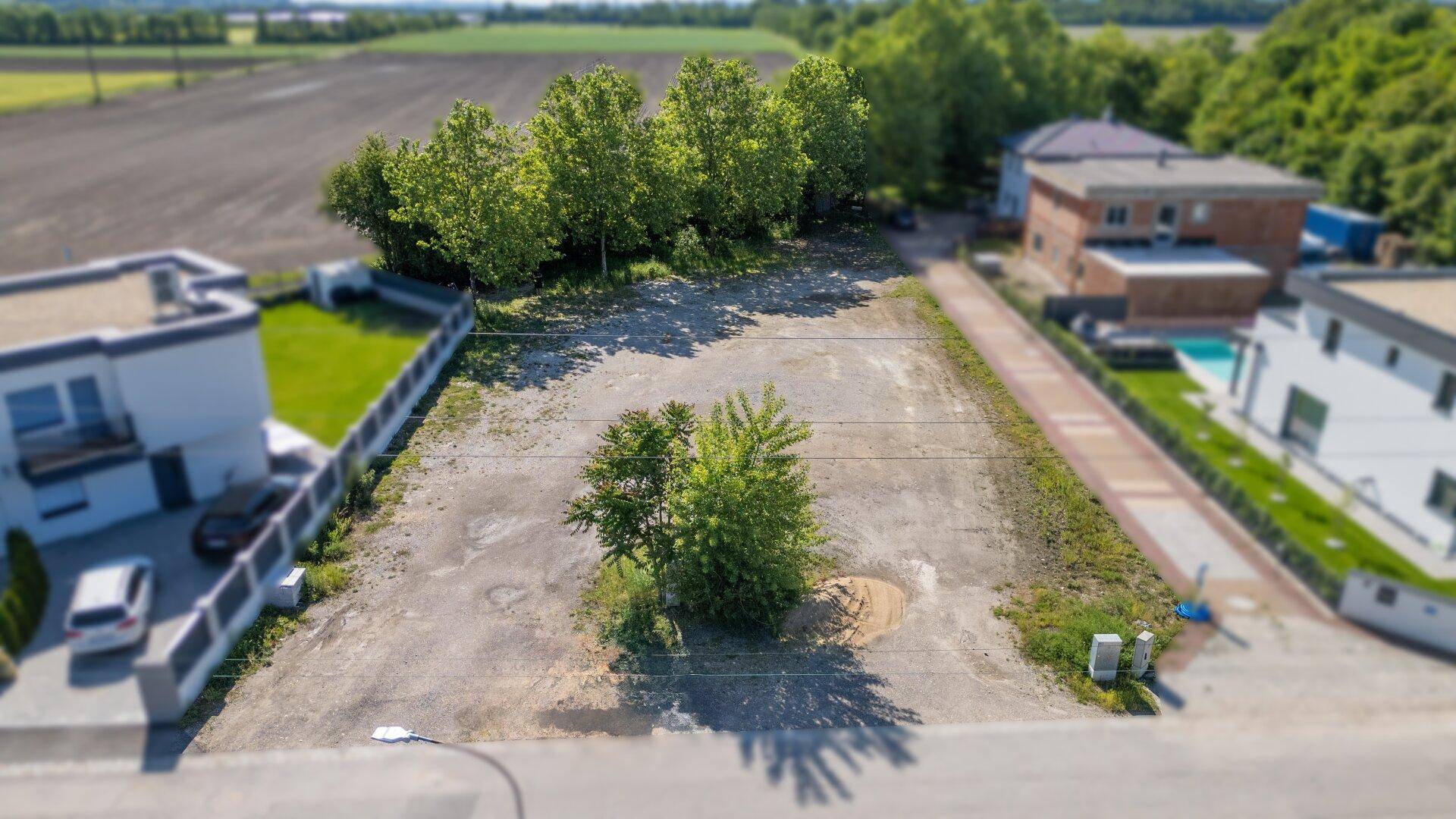 Weitläufiges Baugrundstück aus der Vogelperspektive mit angrenzenden Feldern, Häusern und einem Pool.