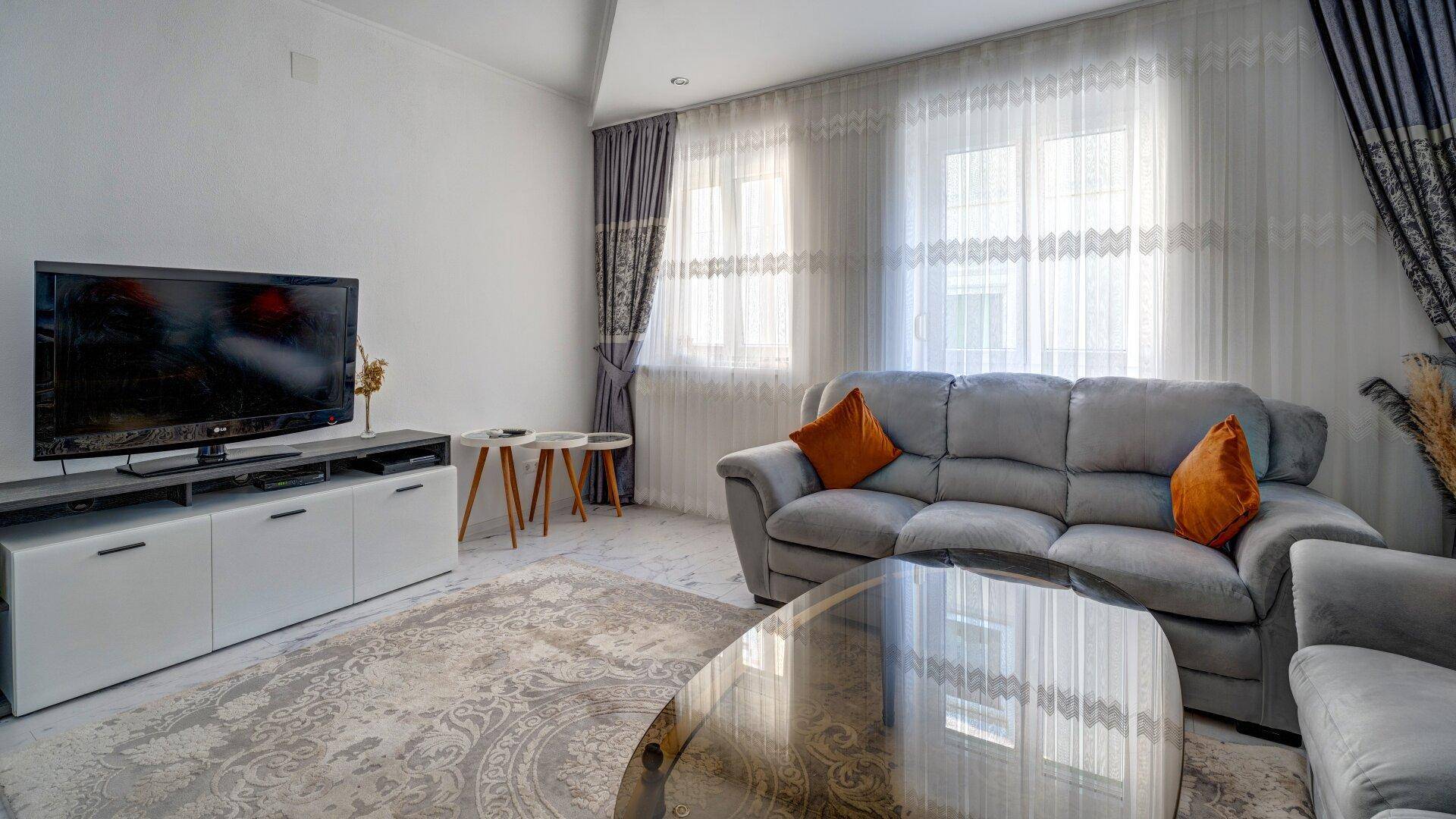 Helles Wohnzimmer mit Fernseher, bequemen Sofas und großen Fenstern für viel Tageslicht.