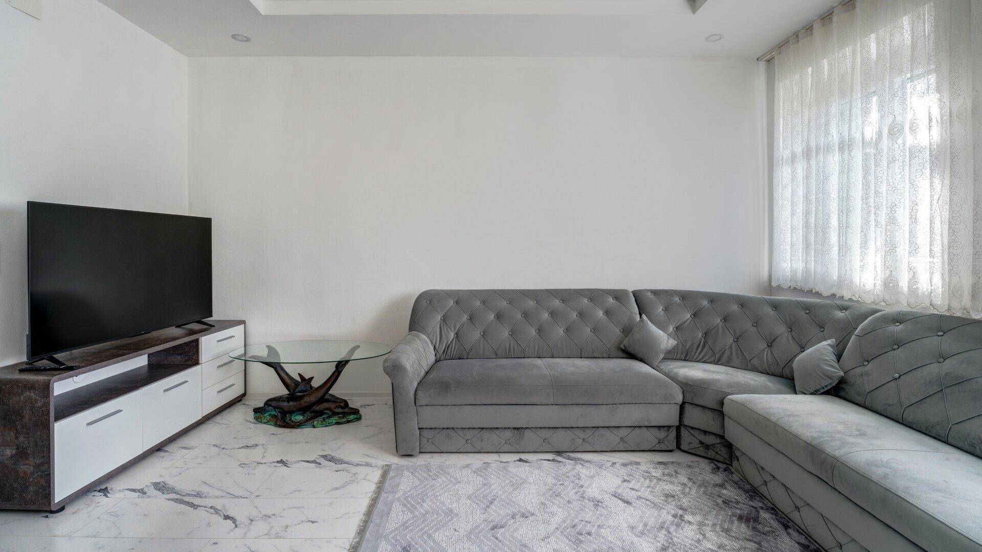 Geräumiges Wohnzimmer mit großem L-förmigem Sofa, Fernseher und modernem Couchtisch.