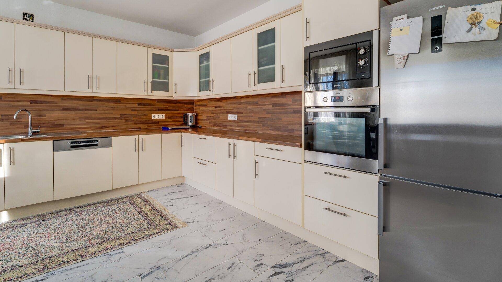 Moderne Küche mit cremefarbenen Schränken, Holzwandverkleidung und integrierten Geräten.