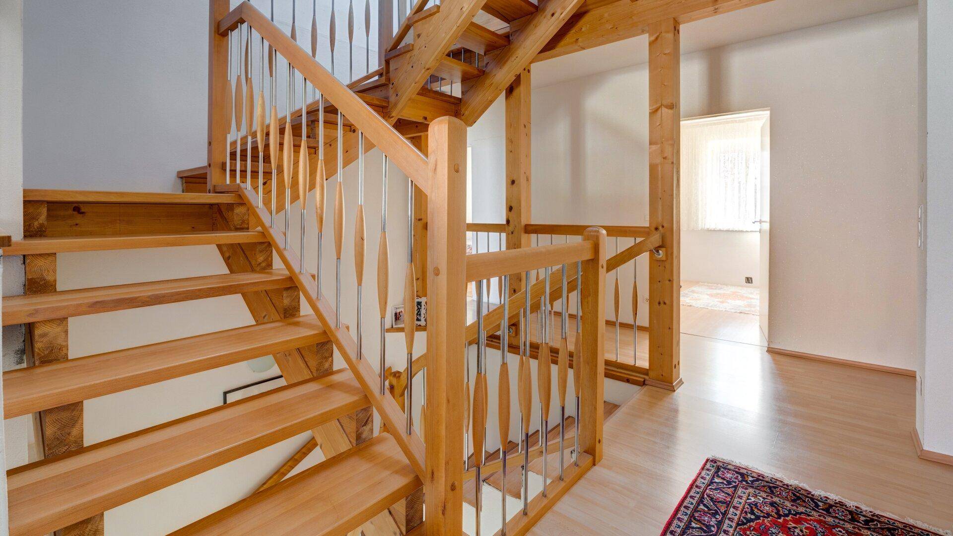 Helle Holztreppe mit modernen Geländern führt in die obere Etage, offener Wohnbereich.