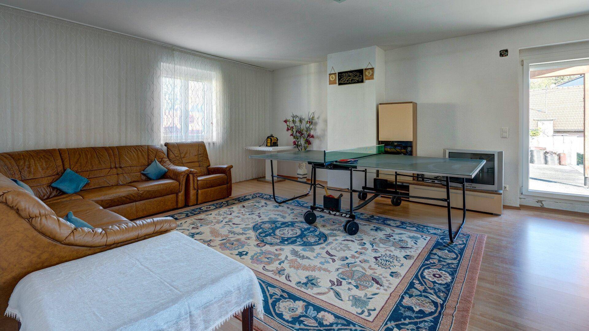 Geräumiges Wohnzimmer mit Ledersofa, einem Tischtennistisch und Zugang zur Terrasse.