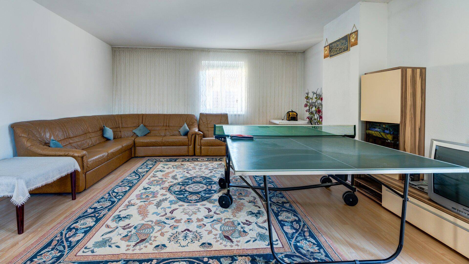 Helles Wohnzimmer mit braunem Ledersofa und einem Tischtennistisch für Freizeitaktivitäten.