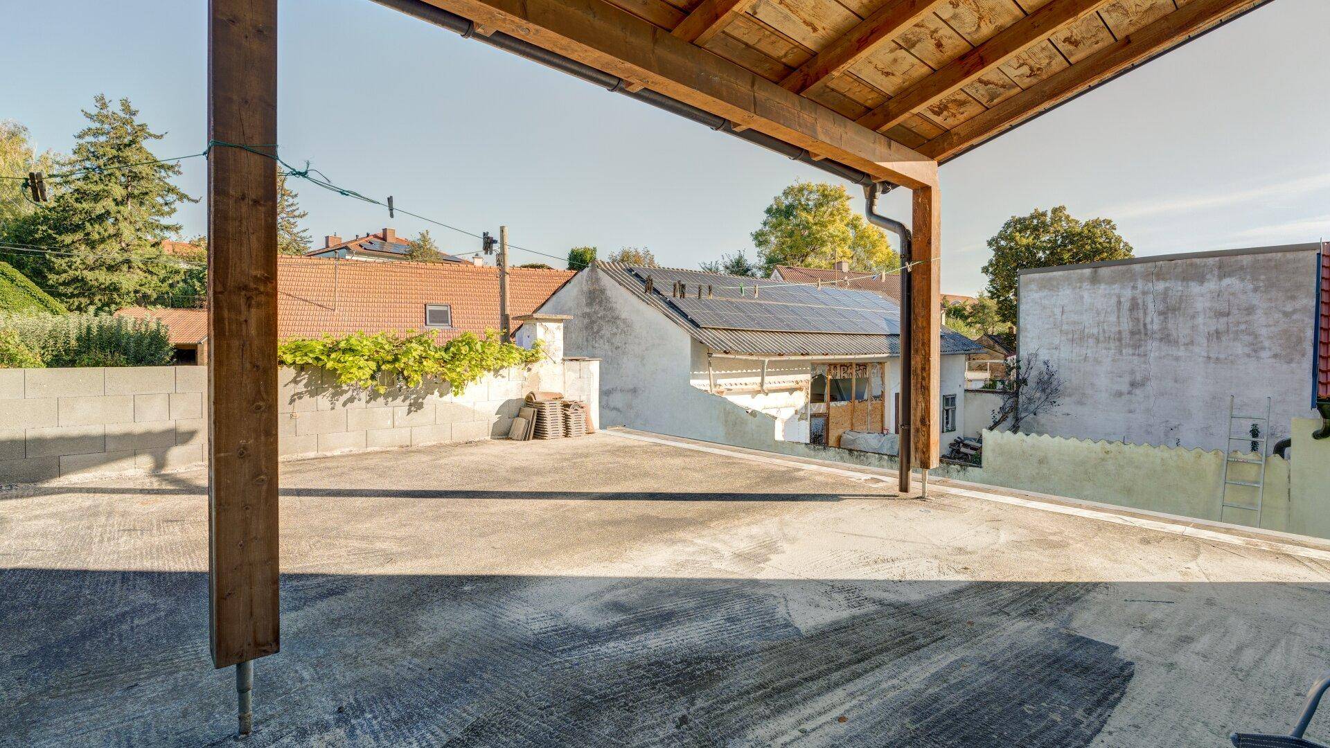 Überdachte Terrasse mit Betonboden und Blick auf die umliegenden Häuser und Solaranlagen.