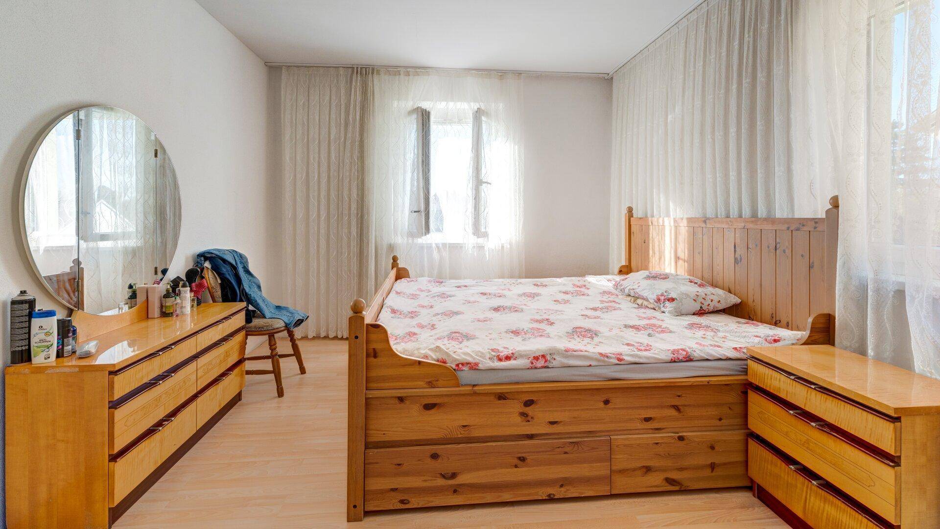 Geräumiges Schlafzimmer mit Holzdoppelbett, Kommode mit Spiegel und viel Tageslicht.