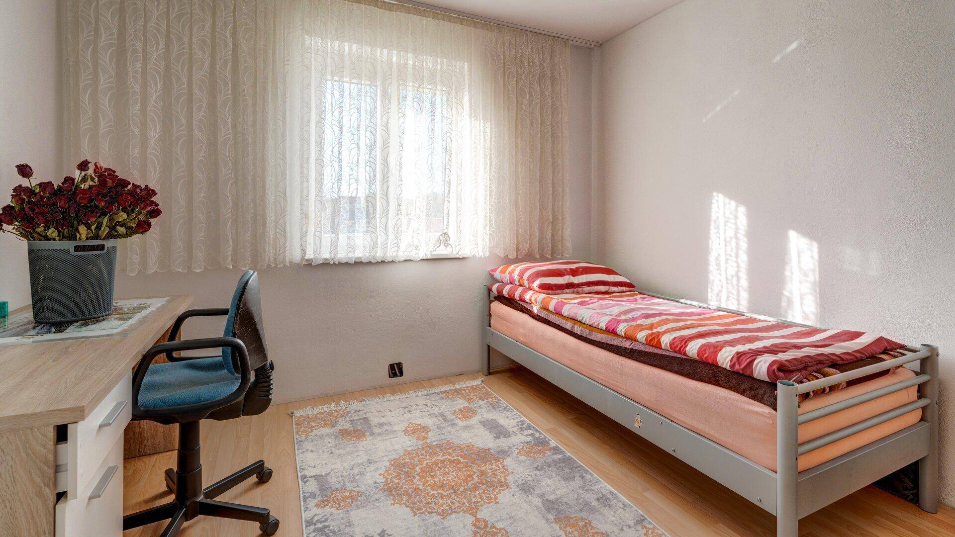 Gemütliches Schlafzimmer mit Einzelbett, Schreibtisch und viel Tageslicht durch das Fenster.
