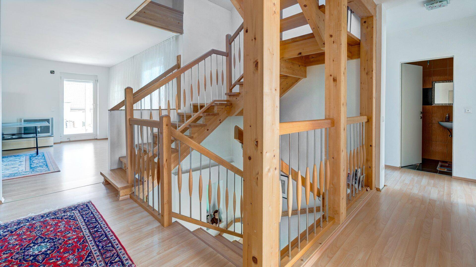 Geräumiger Flur mit Holztreppe und Geländer, der zu weiteren Räumen führt.