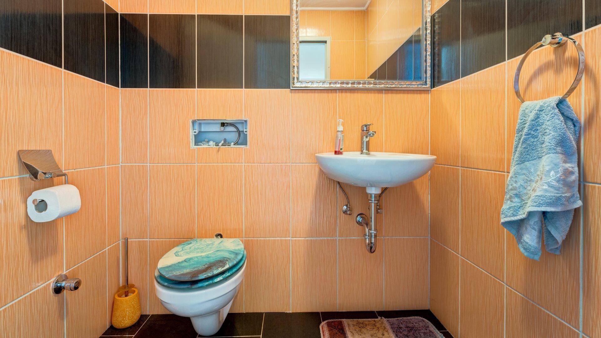 Kleines Gäste-WC mit orange-schwarzen Fliesen, Toilette und Einzelwaschbecken.