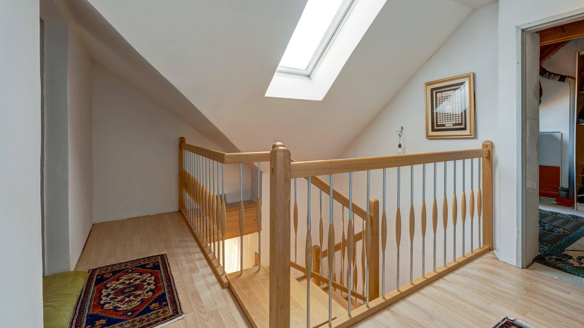 Dachgeschoss-Treppenbereich mit Holzgeländer und einem Dachfenster für natürliches Licht.