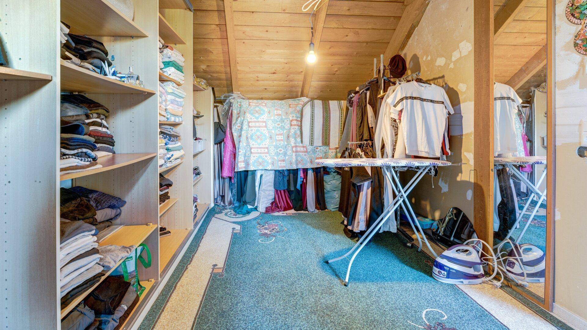 Praktischer Abstellraum im Dachgeschoss mit Regalen, Kleiderstangen und Holzdecke.