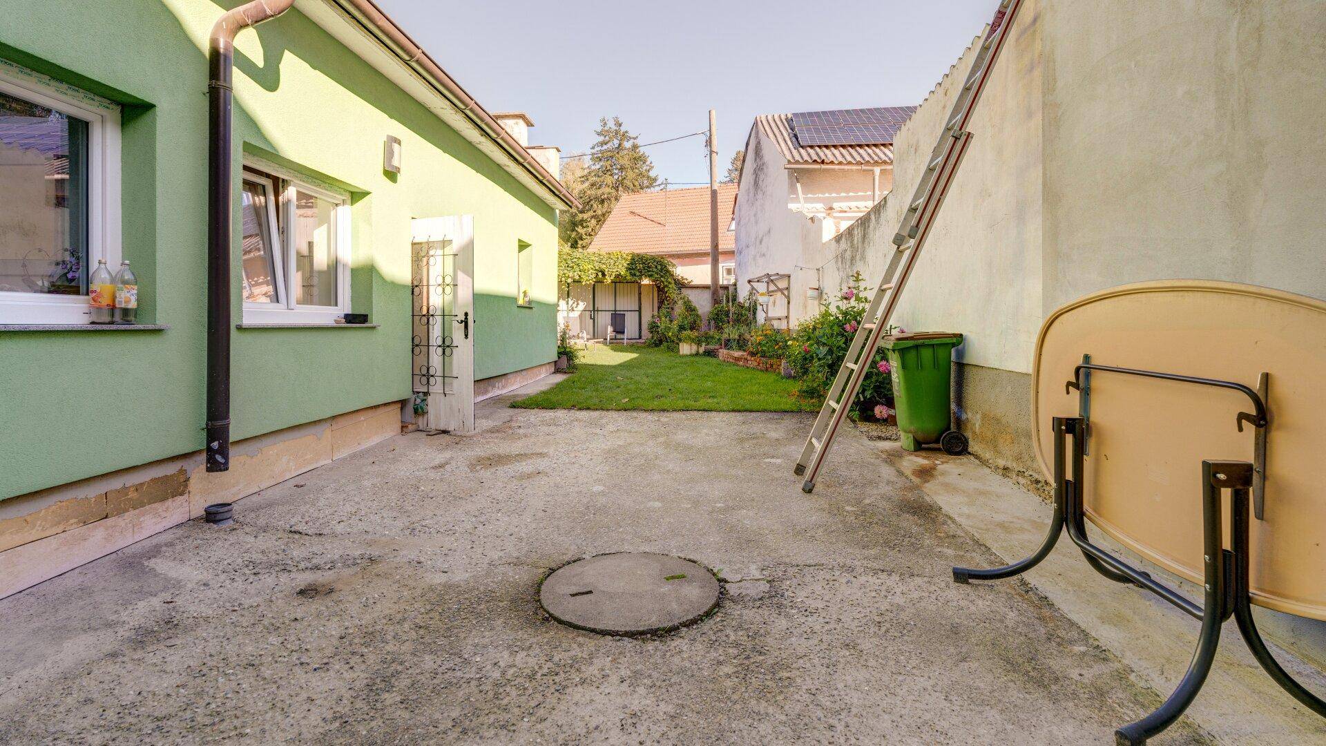 Hinterhof mit Betonfläche, kleinem Rasenbereich und grün gestrichener Hausfassade.
