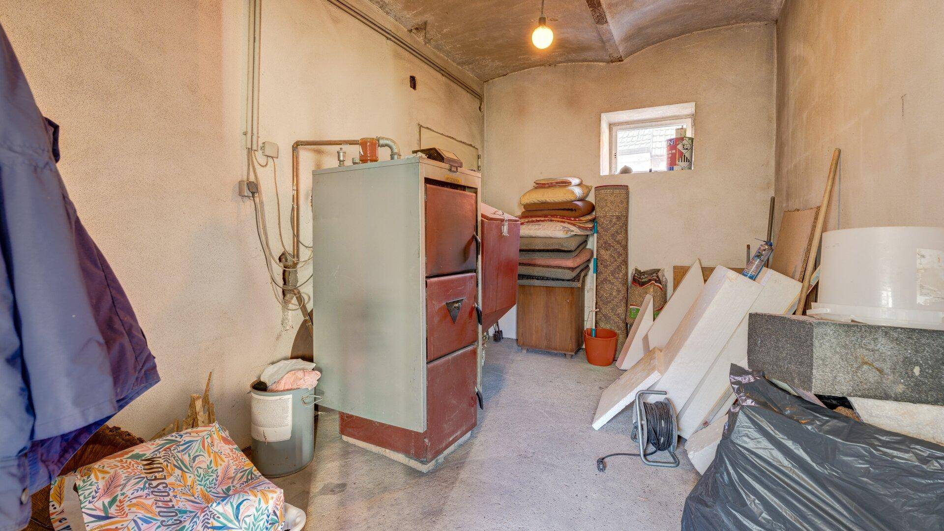 Kellerraum mit Heizungsanlage, sichtbaren Rohren und Lagerflächen für diverse Gegenstände.