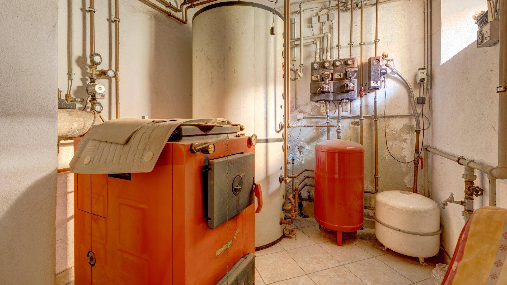 Hauswirtschaftsraum im Keller mit großem Heizkessel, Warmwasserspeicher und vielen Rohren.