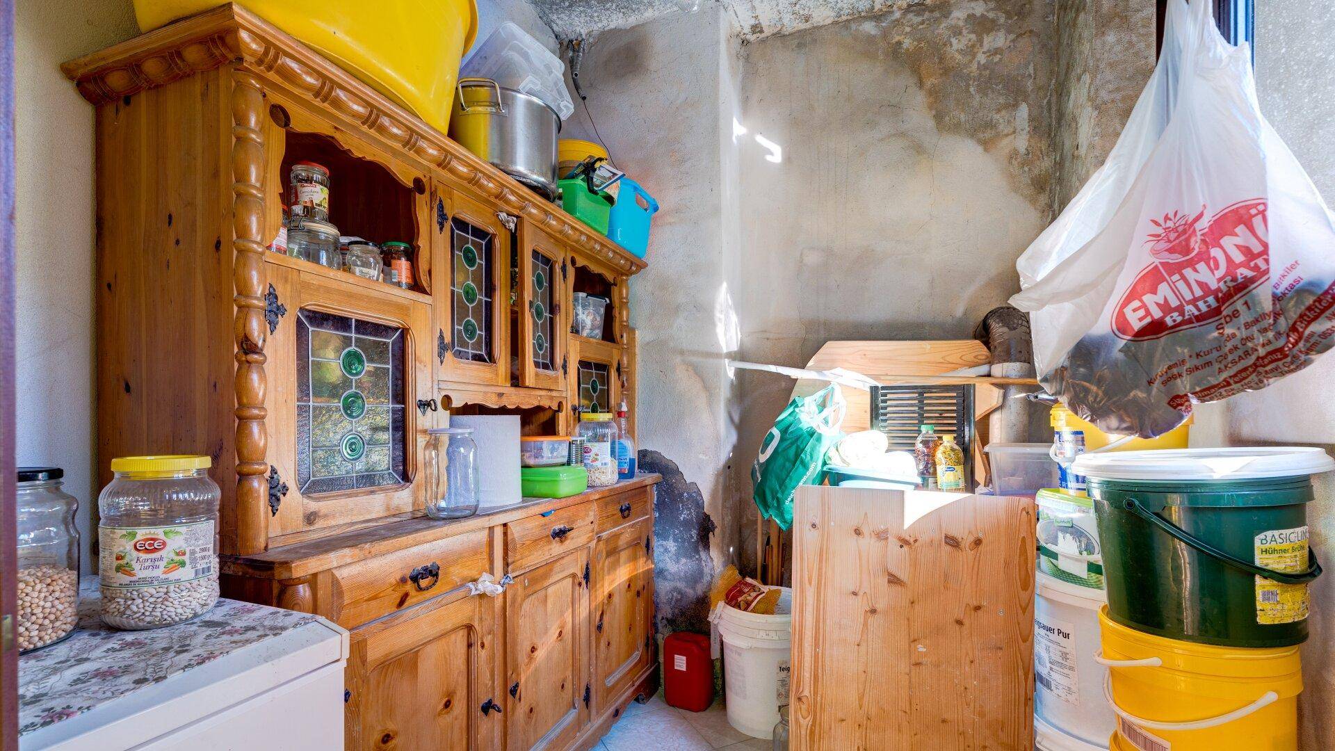 Unaufgeräumter Abstellraum mit altem Holzschrank und vielen gelagerten Haushaltsgegenständen.