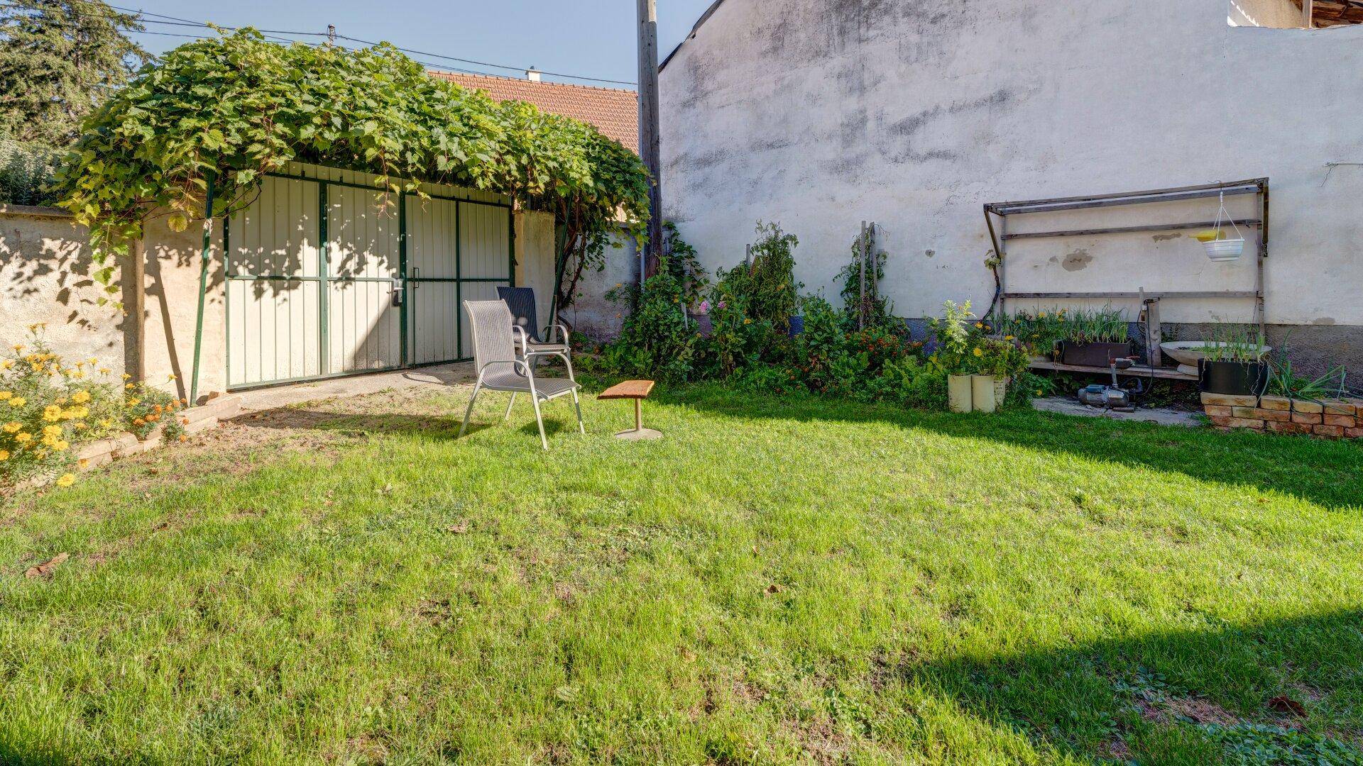 Grüner Gartenbereich mit Rasenfläche, bewachsenem Tor und einfacher Sitzgelegenheit im Freien.