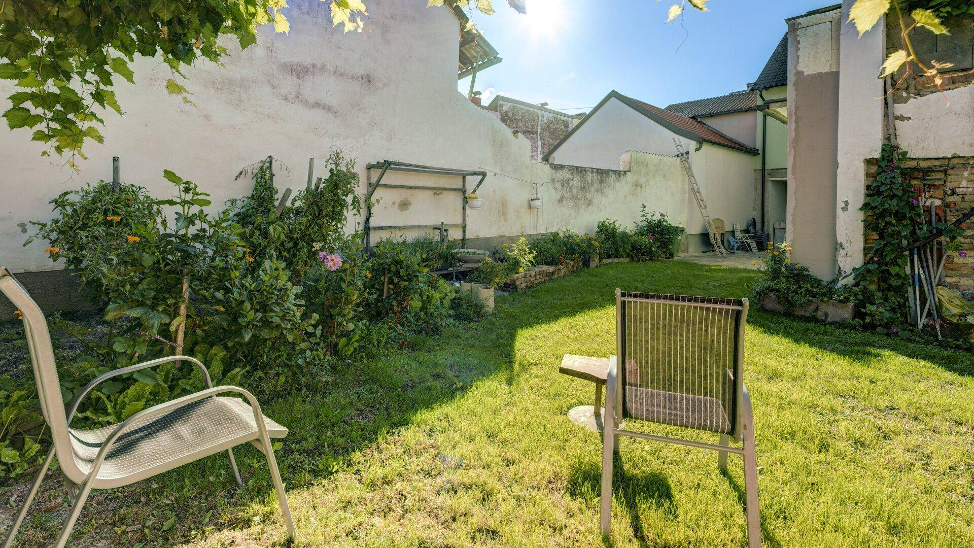 Sonniger Garten mit Rasenfläche und bequemen Gartenstühlen, ideal zum Entspannen.
