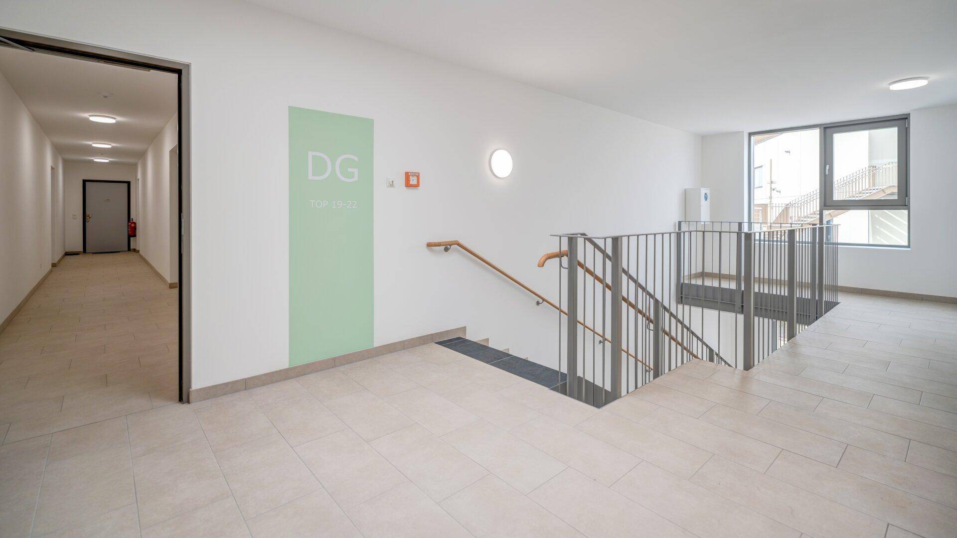 Heller Treppenhausbereich mit Fliesenboden, Geländer und Zugang zu den oberen Etagen.