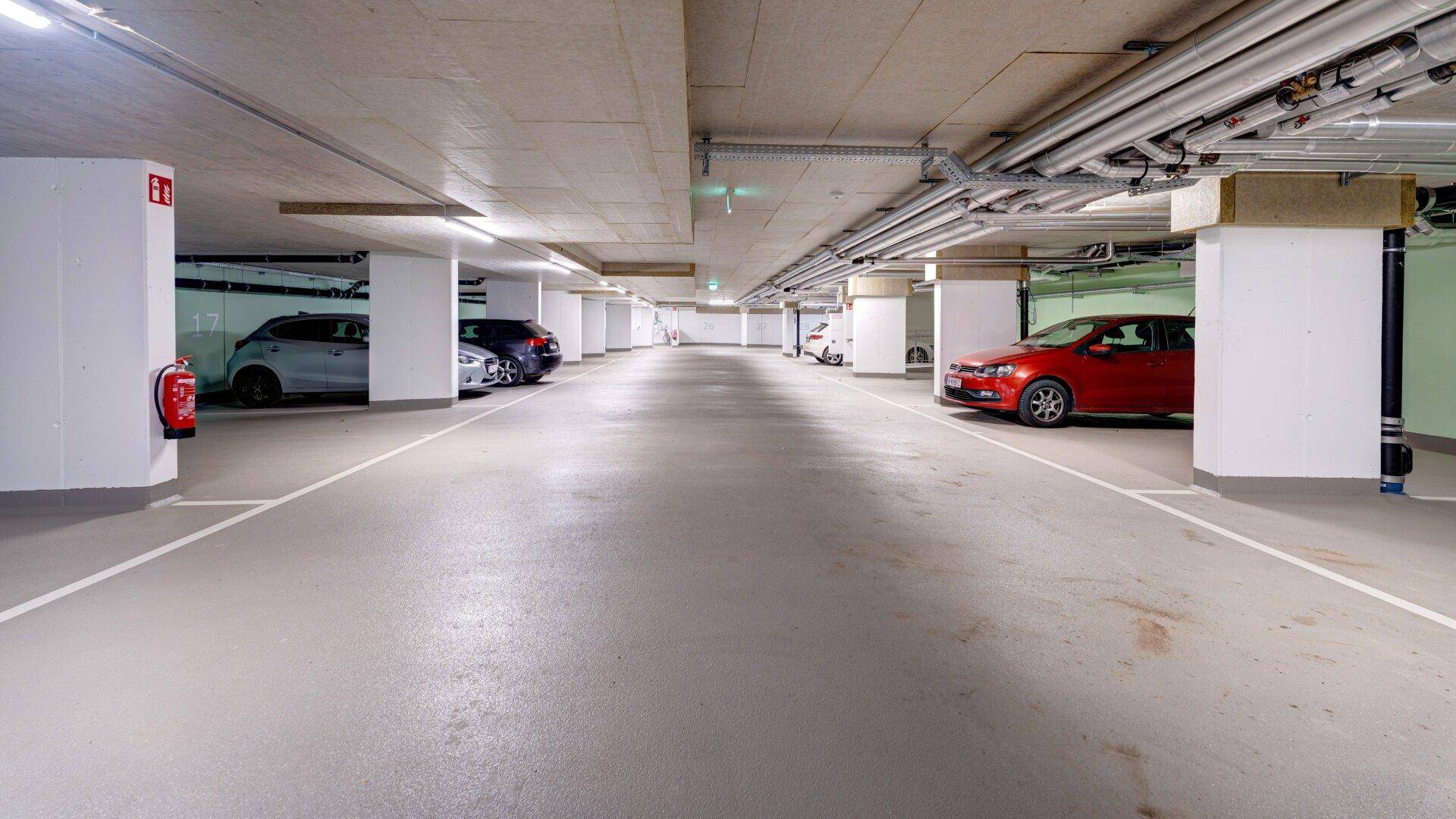 Helle Tiefgarage mit mehreren geparkten Autos und gut sichtbaren Säulenstrukturen.