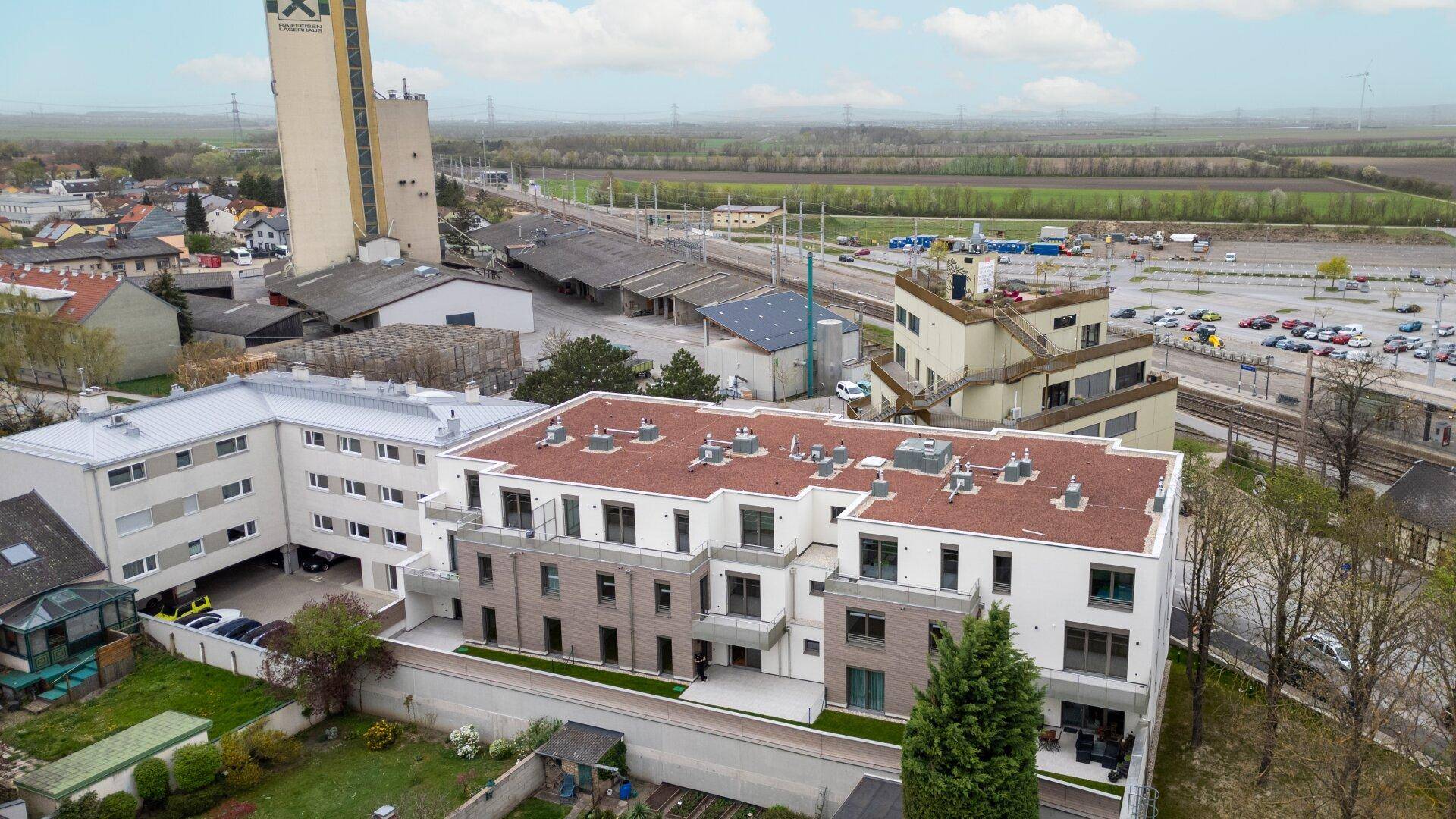 Luftaufnahme einer Wohnanlage mit Blick auf Industriegebäude und weite Felder im Hintergrund.