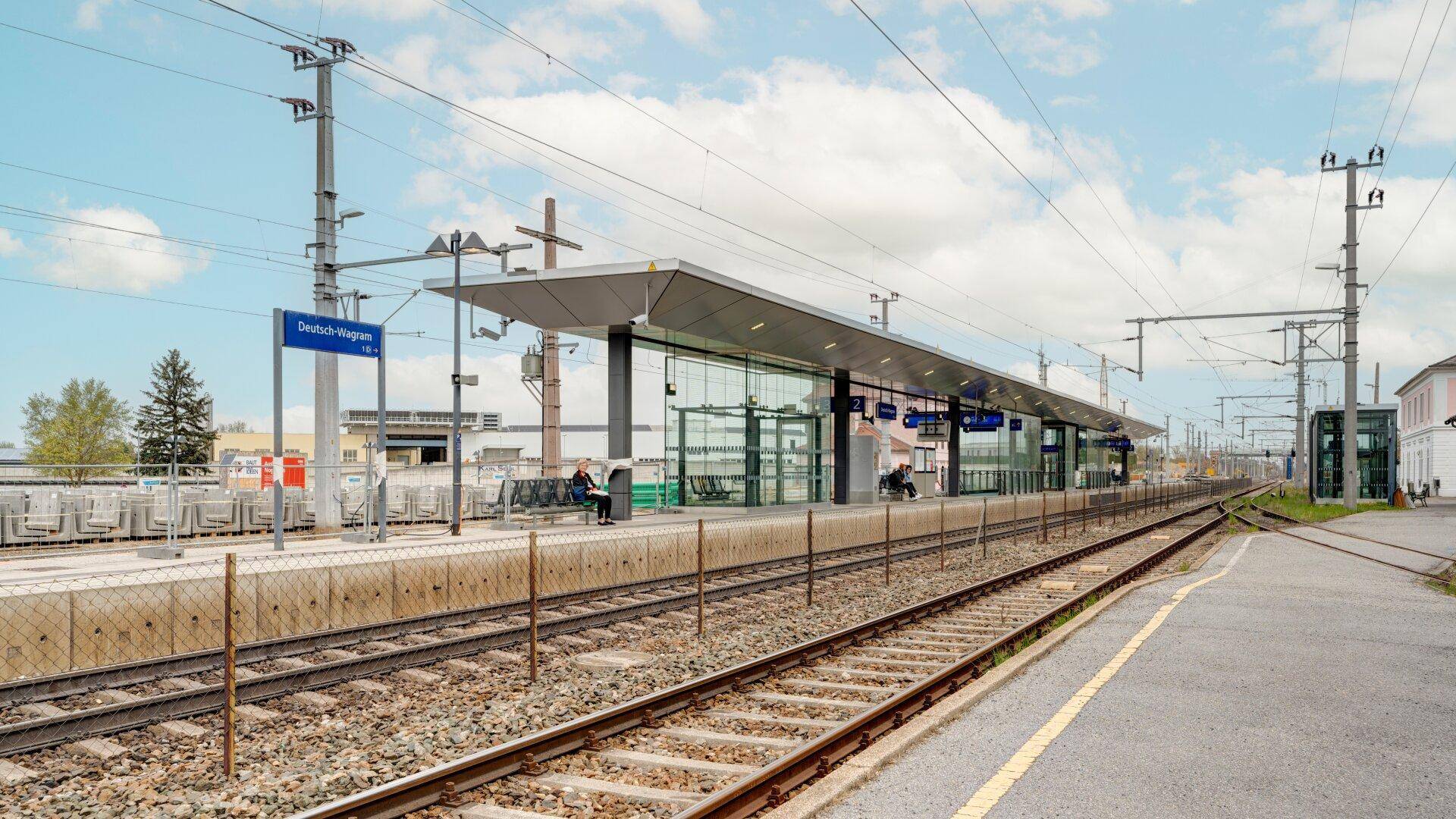 Moderner Bahnhof mit Bahnsteigen, Gleisen und Oberleitungen unter einem weiten blauen Himmel.