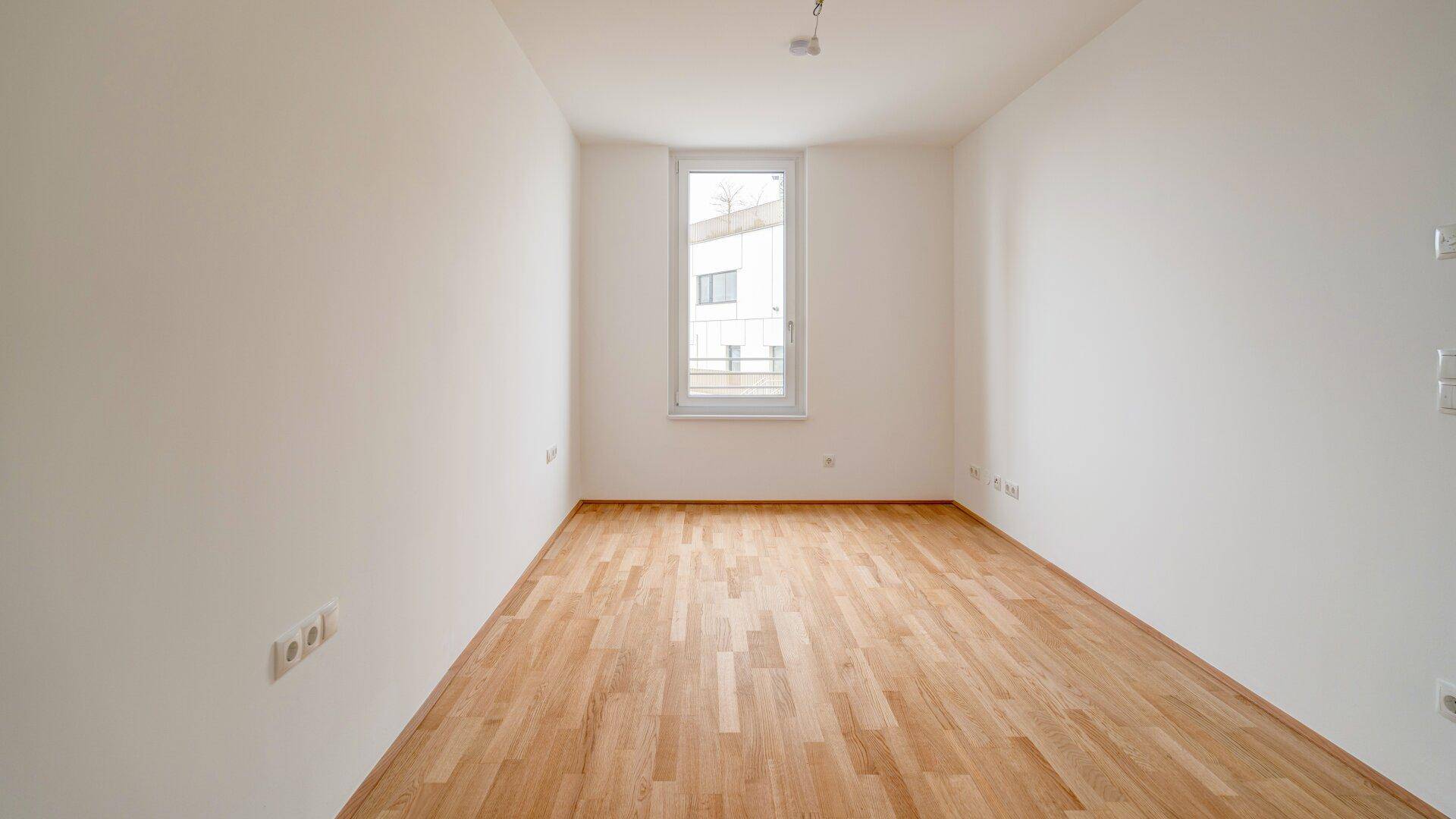 Heller, leerer Raum mit Parkettboden und einem hohen Fenster, ideal als Schlaf- oder Arbeitszimmer.