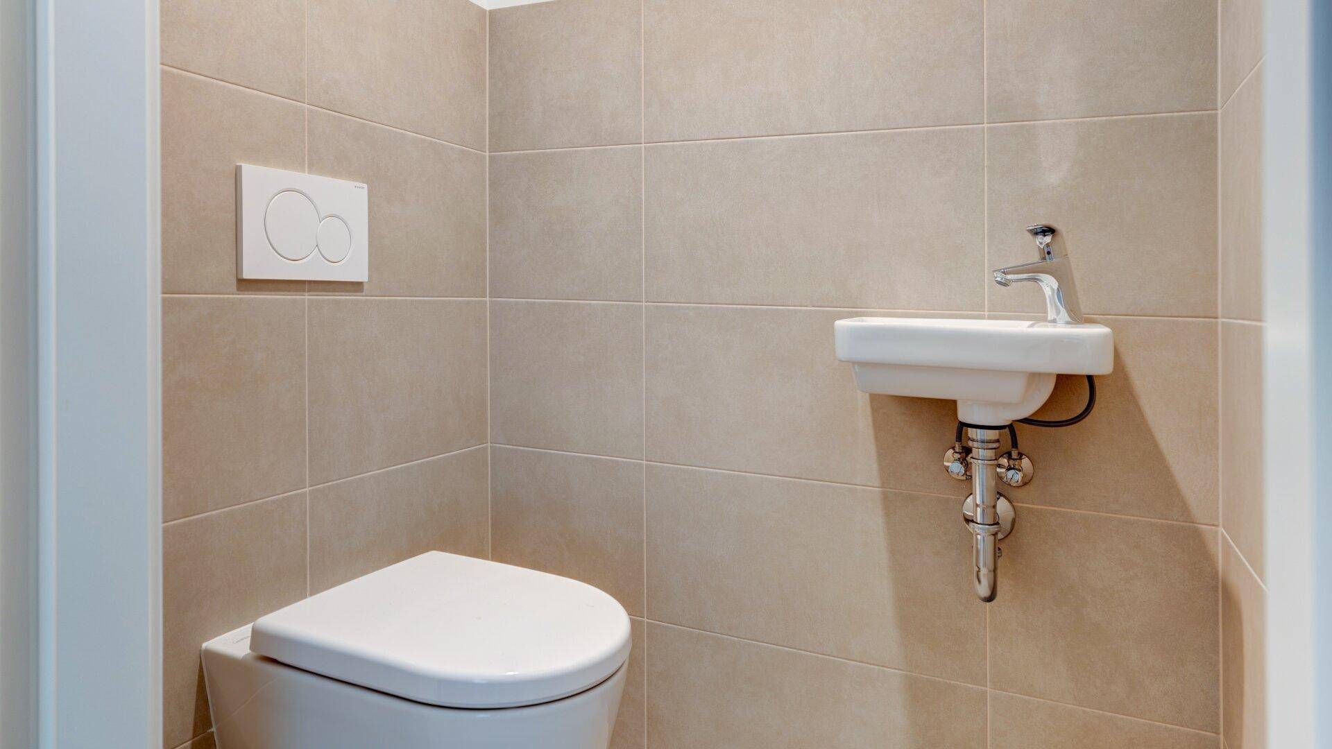Modernes Gäste-WC mit beigefarbenen Fliesen, wandhängender Toilette und kleinem Waschbecken.