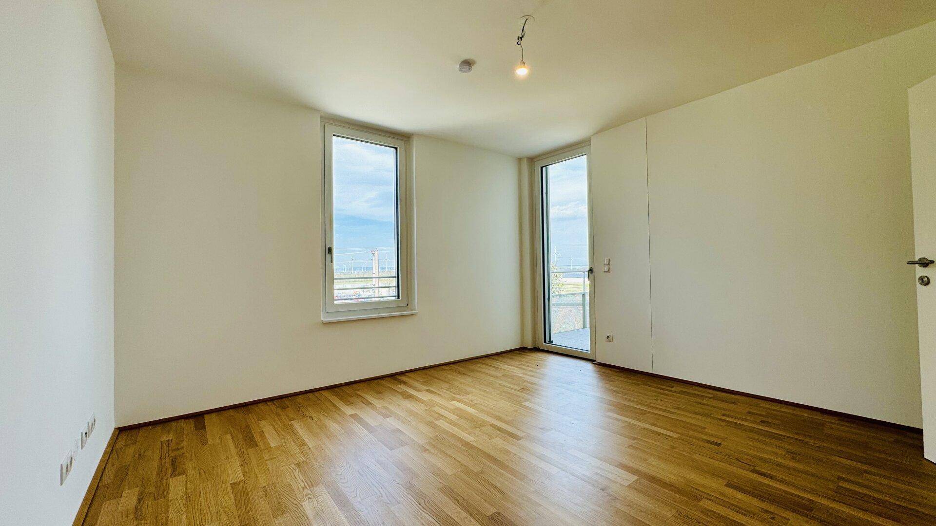Helles Schlafzimmer mit Parkettboden und Zugang zu einem Balkon oder einer Terrasse.