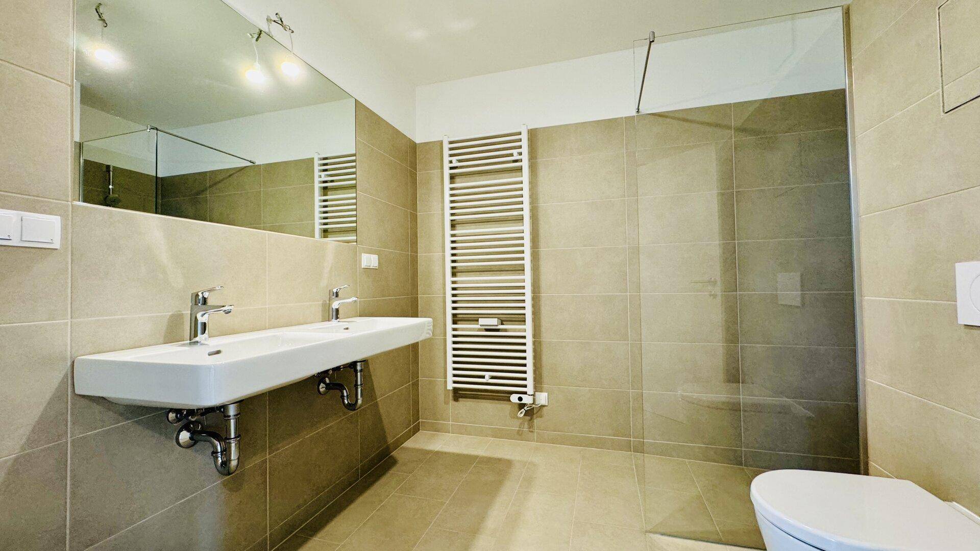 Modernes Badezimmer mit Doppelwaschbecken, großer Dusche und beheiztem Handtuchhalter.