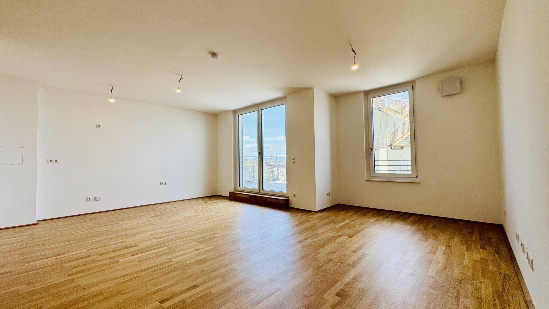 Geräumiges Wohnzimmer mit Parkettboden, großen Fenstern und Zugang zu einem Außenbereich.