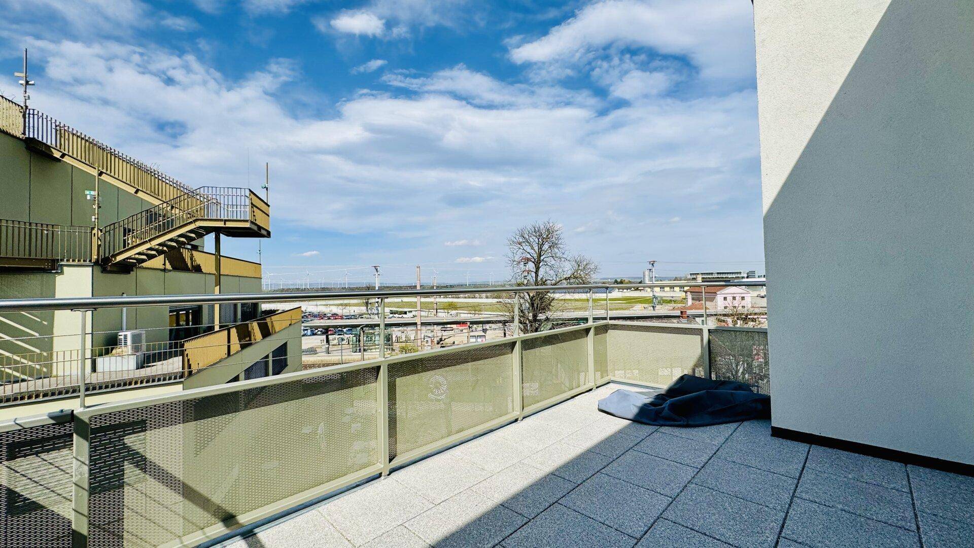 Geräumiger Balkon mit Fliesenboden und Blick auf die Umgebung und Bahngleise.