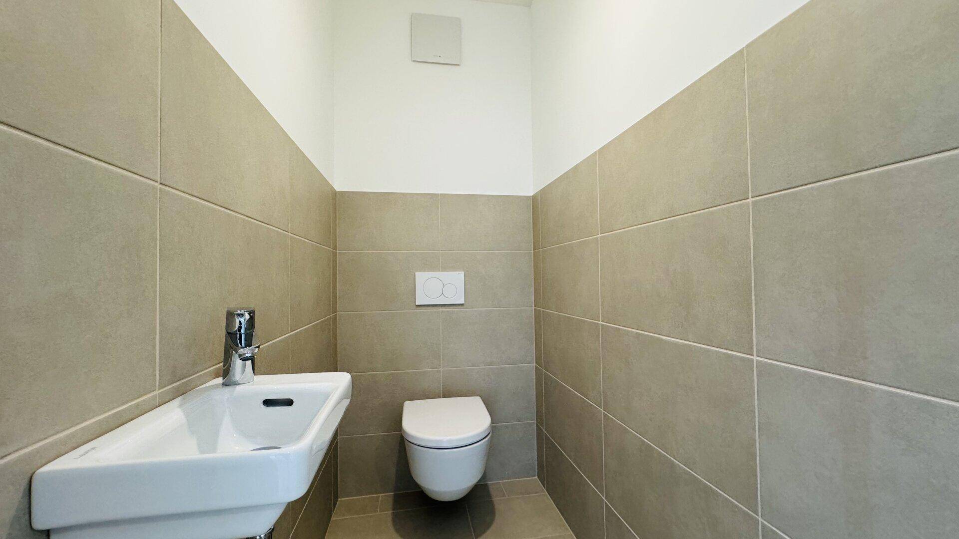 Modernes Gäste-WC mit Wand-WC und kleinem Waschbecken, halbhoch gefliest.