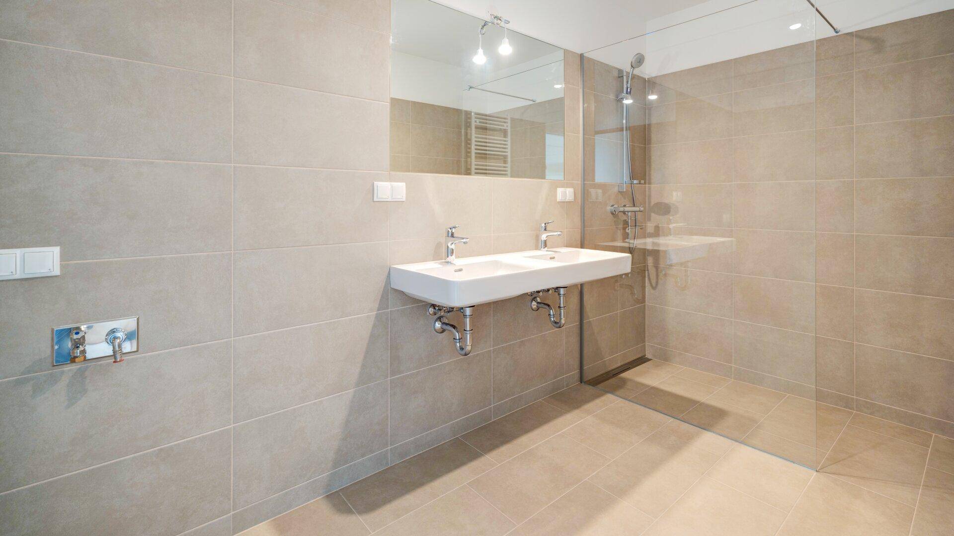 Modernes Badezimmer mit doppelten Waschbecken, großer begehbarer Dusche und beigefarbenen Fliesen.