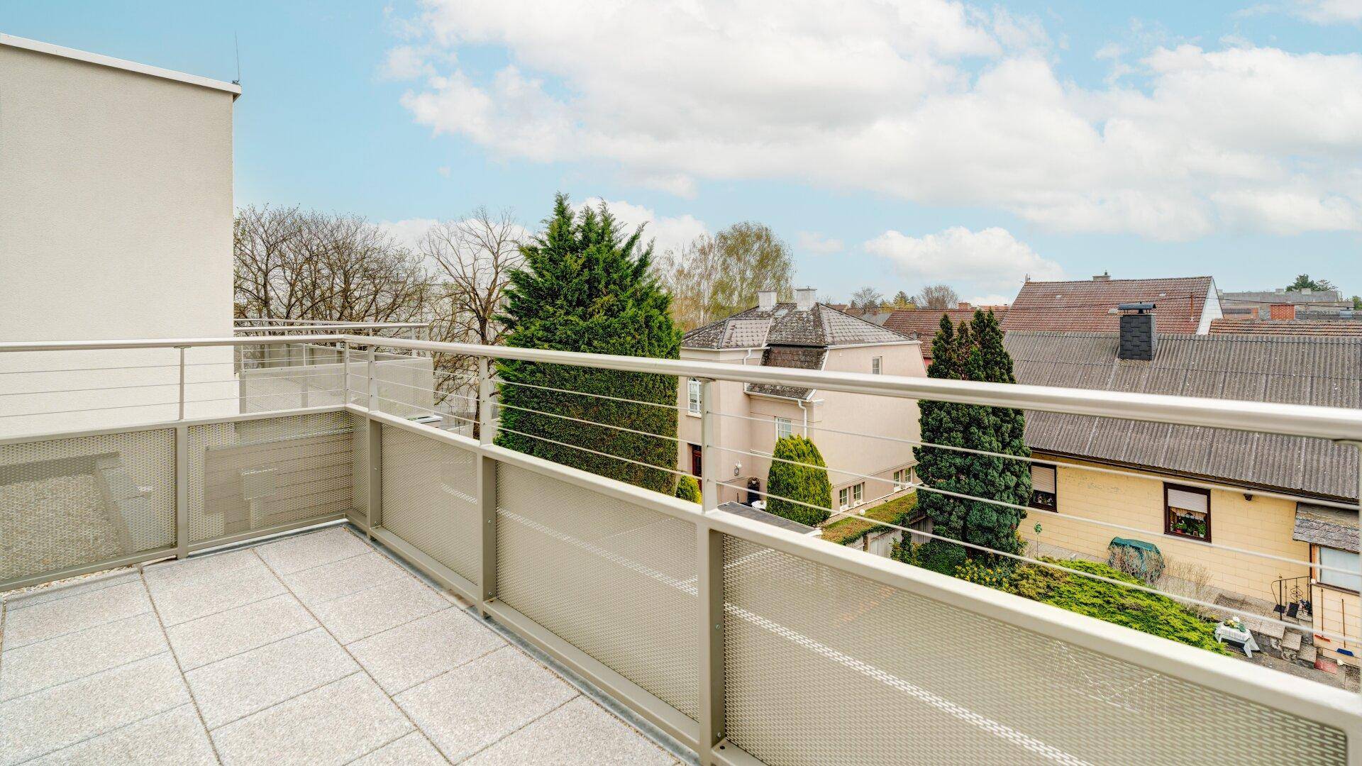 Geräumiger Balkon mit Fliesenboden und Blick auf die umliegende Wohngegend unter blauem Himmel.