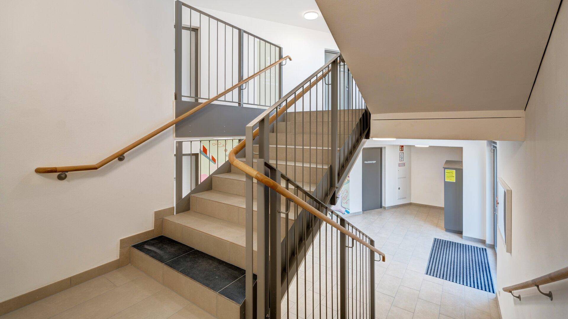 Modernes Treppenhaus mit Metallgeländer und Holzhandlauf in einem Mehrfamilienhaus.