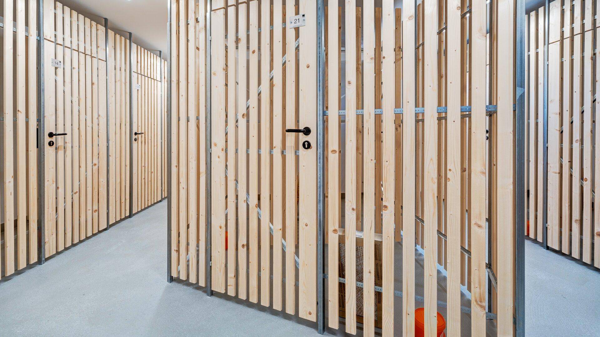 Reihen von individuellen Lagerabteilen mit Holzlattenwänden in einem Kellerbereich.