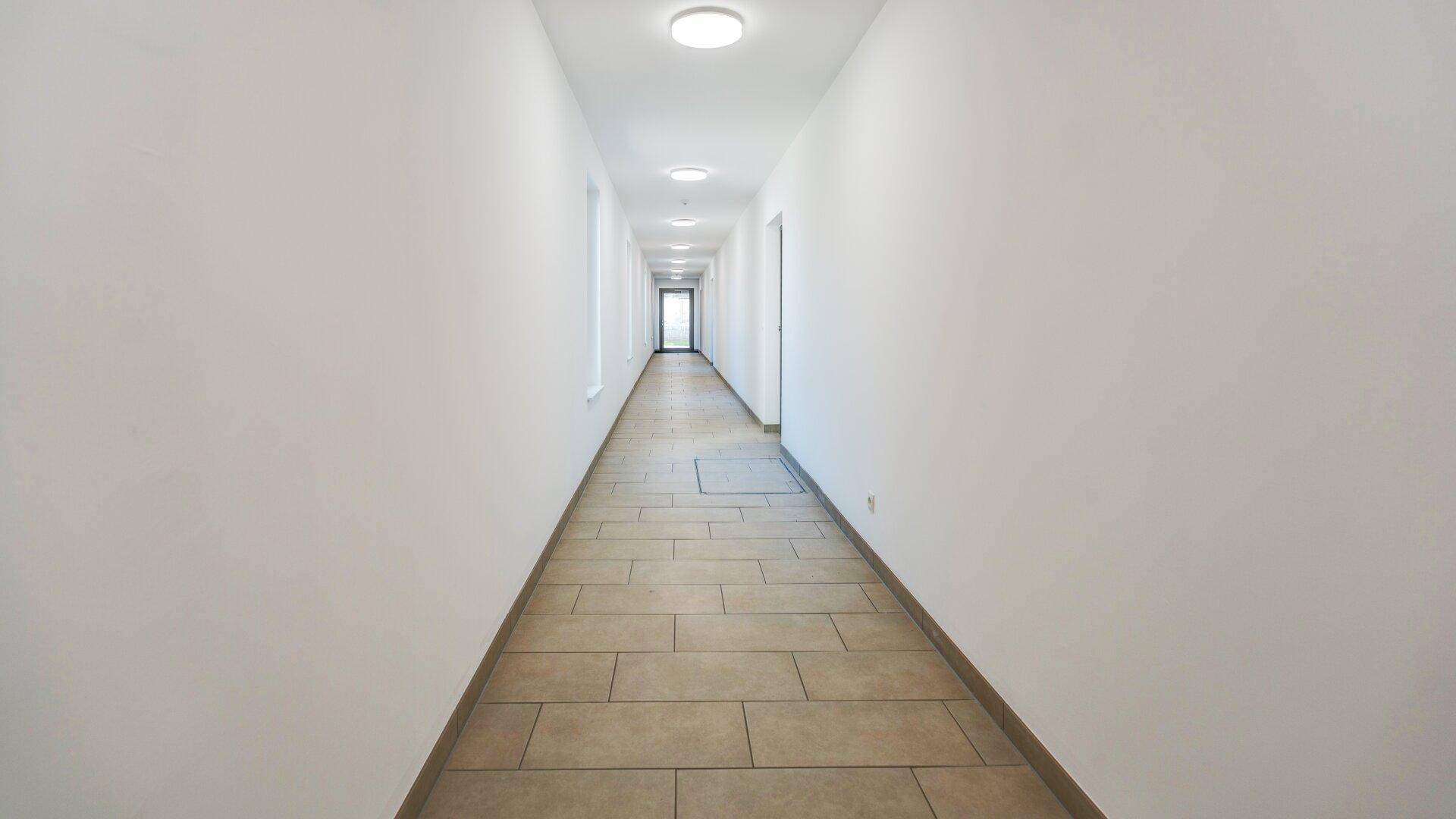 Langer, heller Flur mit modernen Deckenleuchten und Fliesenboden in einem Wohngebäude.