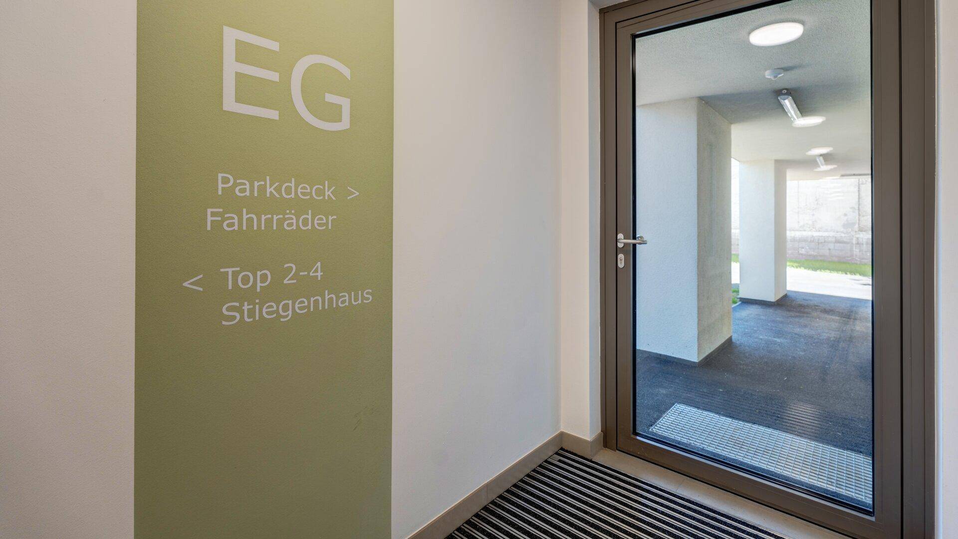 Eingangsbereich mit Hinweisschildern und einer modernen Glastür, die nach draußen führt.