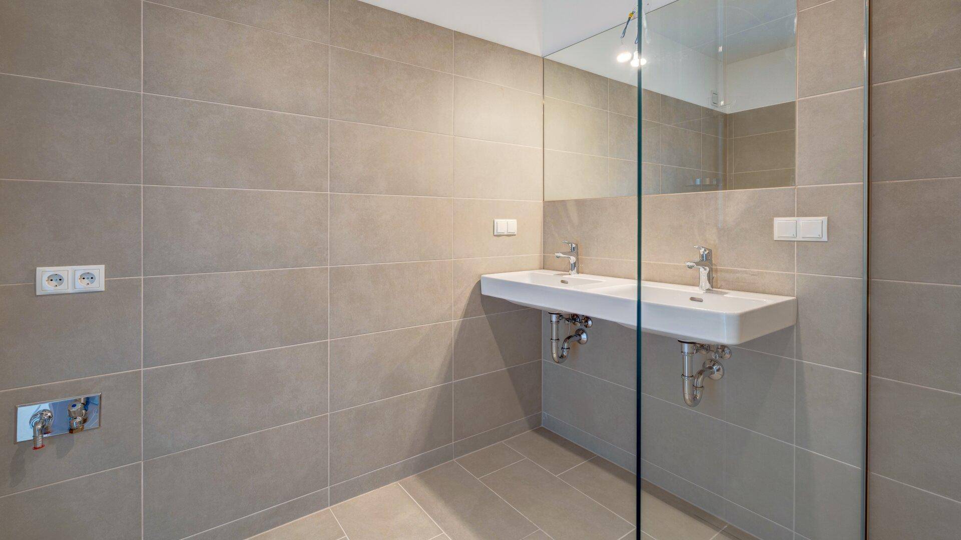 Geräumiges Badezimmer mit Doppelwaschbecken, großem Spiegel und moderner Duschkabine.