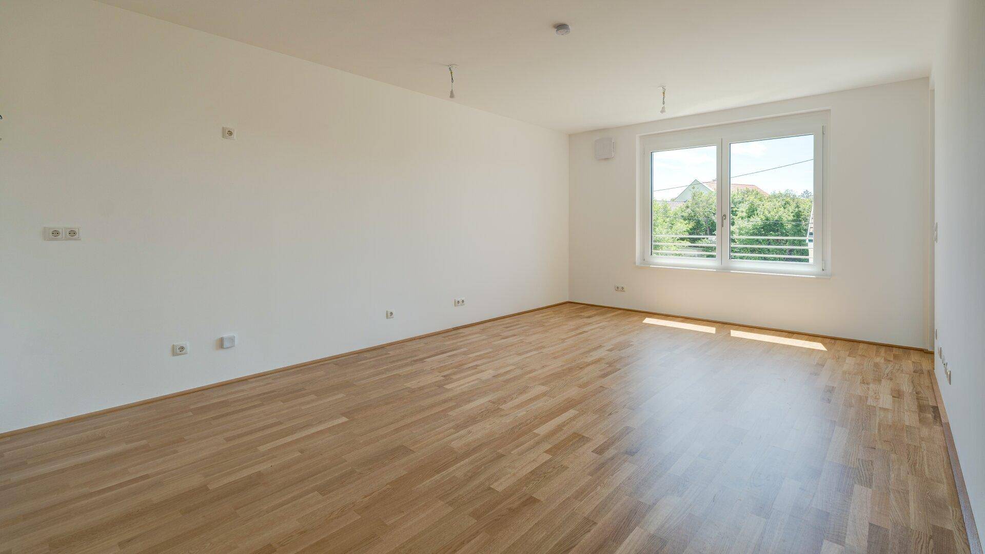 Großes, helles Wohnzimmer mit Parkettboden und weitem Blick ins Grüne durch das Fenster.