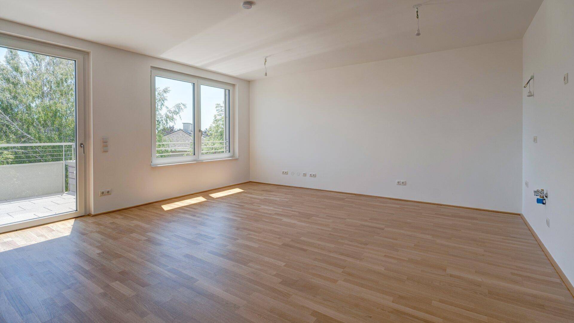 Heller und geräumiger Wohnbereich mit Holzboden und direktem Zugang zum Balkon.