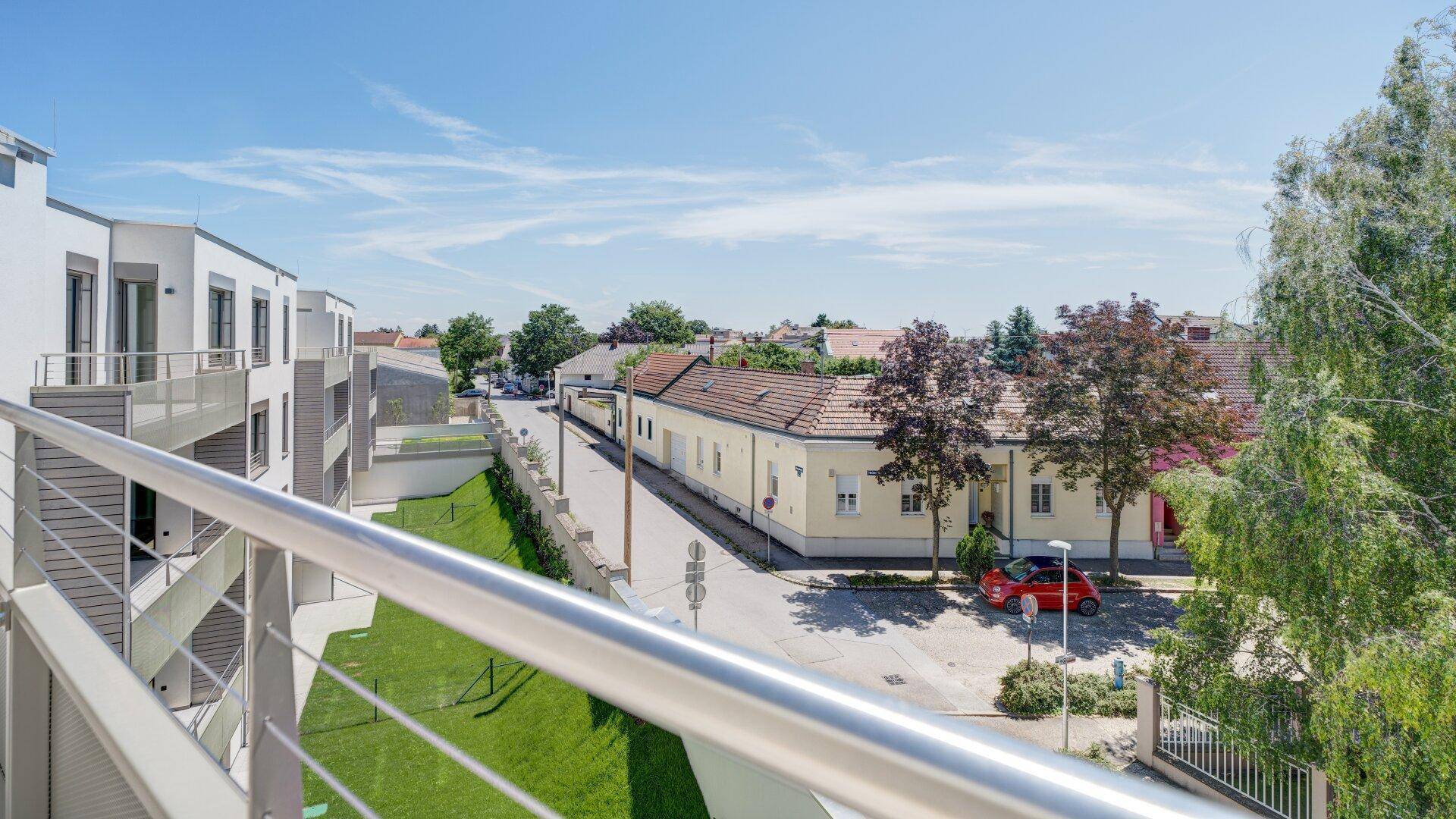 Ausblick vom Balkon auf eine ruhige Wohnstraße mit umliegenden Gebäuden und viel Grün.