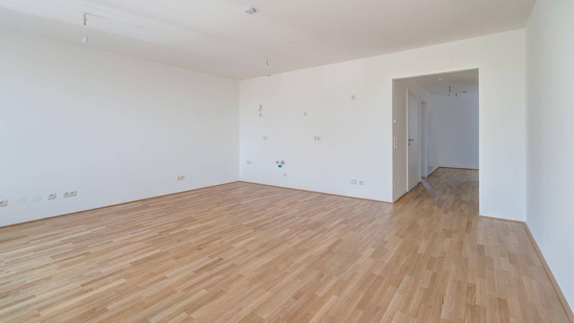 Großzügiger Raum mit Holzboden und weiß gestrichenen Wänden, bietet viel Gestaltungsfreiheit.