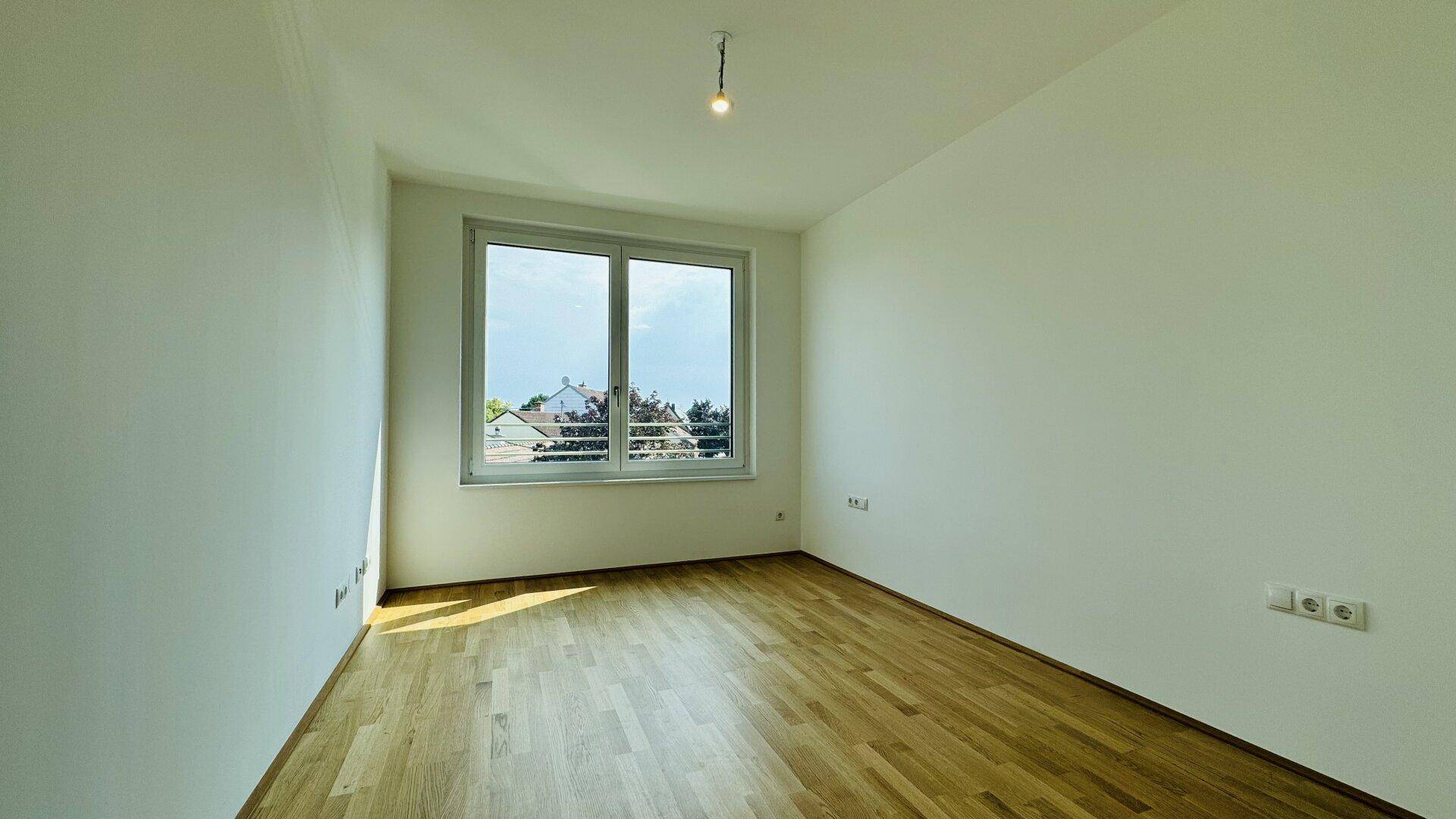 Geräumiges Zimmer mit Holzparkettboden und großen Fenstern für viel Tageslicht.