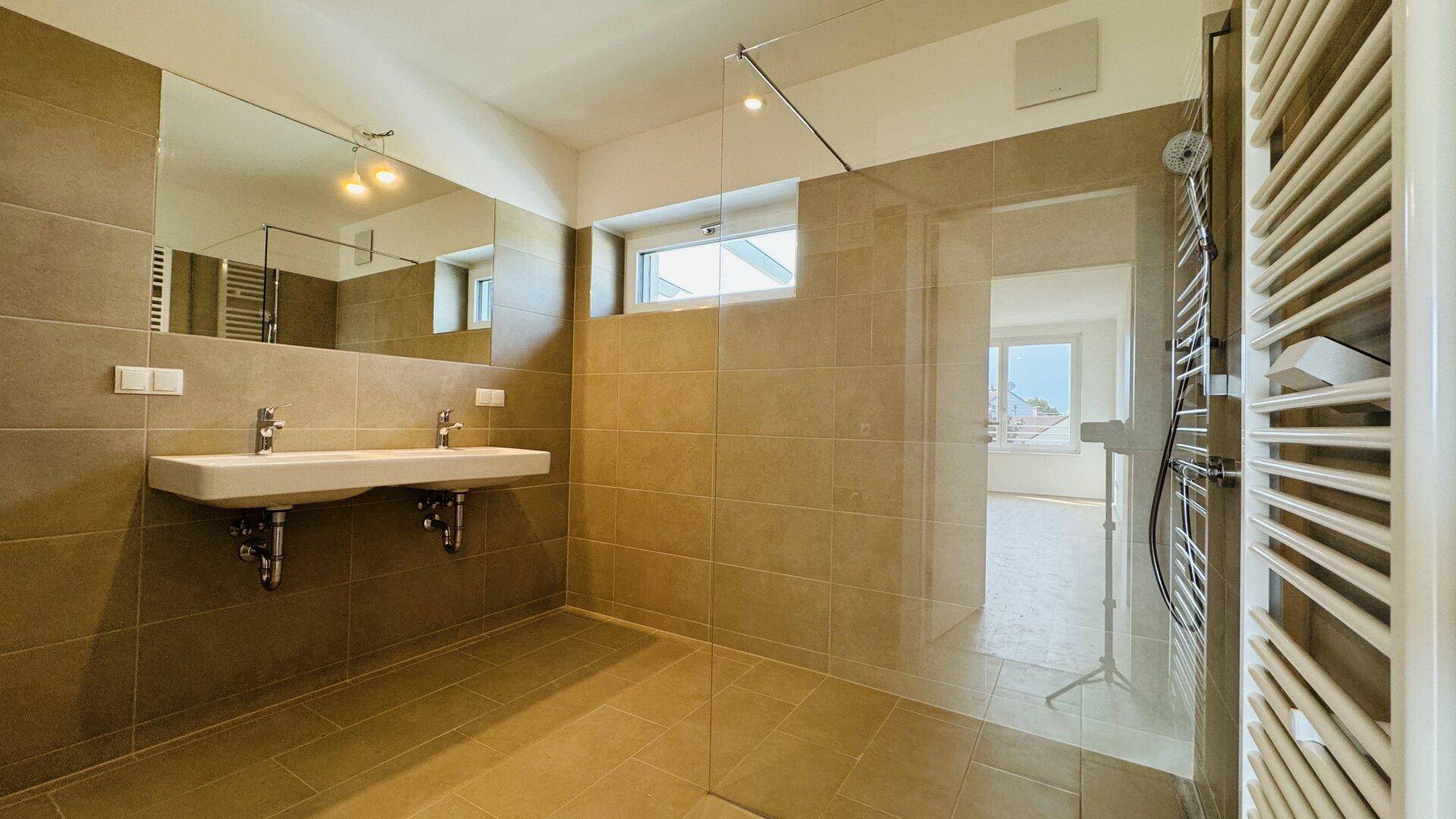 Modernes Badezimmer mit Doppelwaschbecken, großer Dusche und beigefarbenen Fliesen.